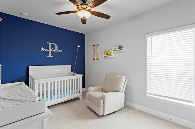 carpeted bedroom featuring baseboards, a ceiling fan, and a crib