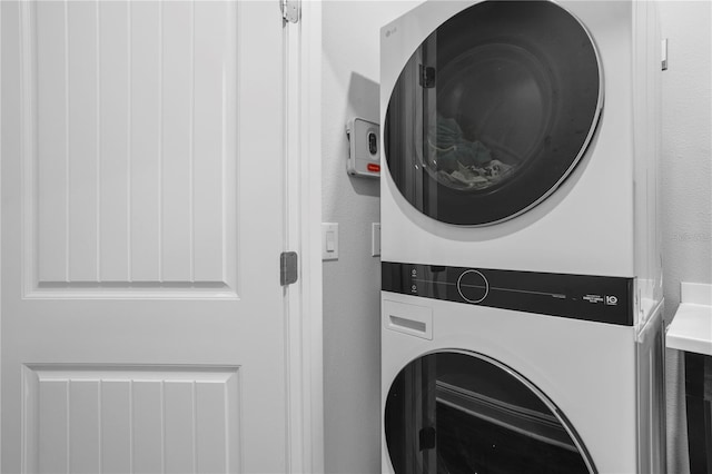 laundry area featuring stacked washer / drying machine, a textured wall, and laundry area