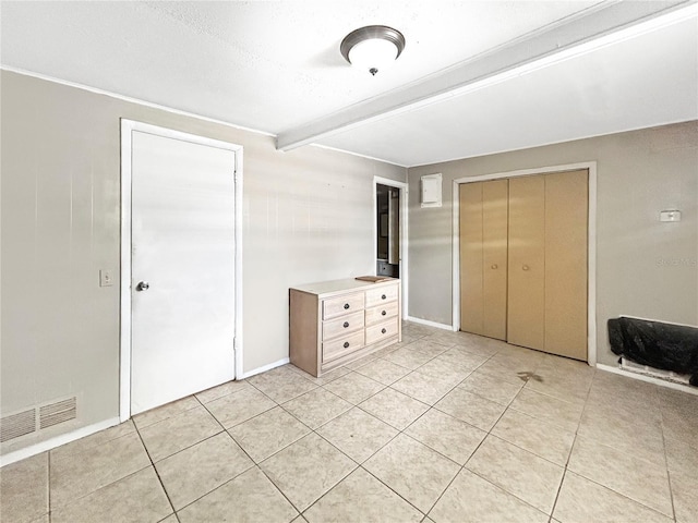 unfurnished bedroom with visible vents, a closet, beam ceiling, light tile patterned flooring, and baseboards