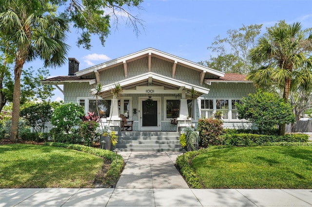 craftsman-style house with a chimney, a porch, and a front yard