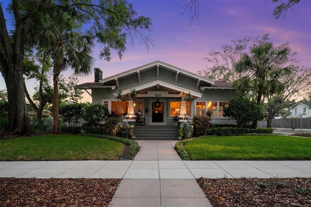 craftsman inspired home with a porch, a front lawn, and a chimney