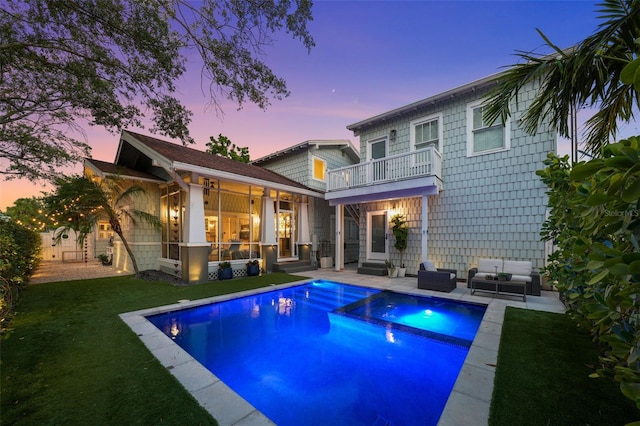 rear view of property with a pool with connected hot tub, outdoor lounge area, a balcony, a lawn, and a patio