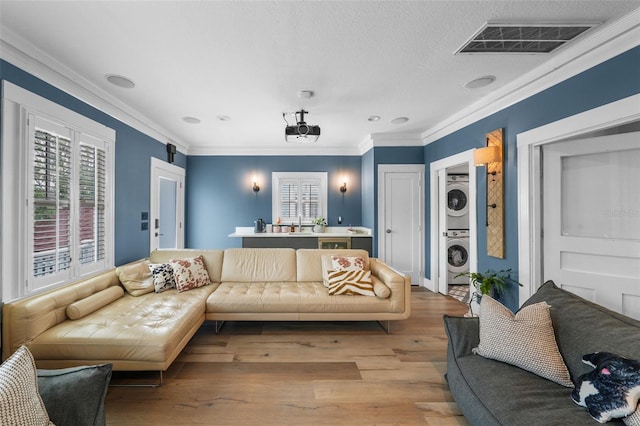 living room featuring ornamental molding, stacked washer and clothes dryer, wood finished floors, and visible vents