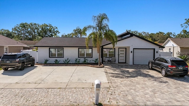 ranch-style home featuring a garage, fence, stucco siding, and driveway