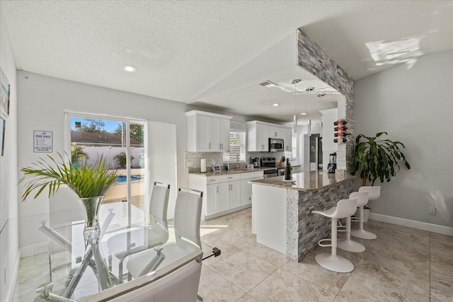kitchen featuring a sink, stone counters, a breakfast bar, stainless steel appliances, and white cabinetry