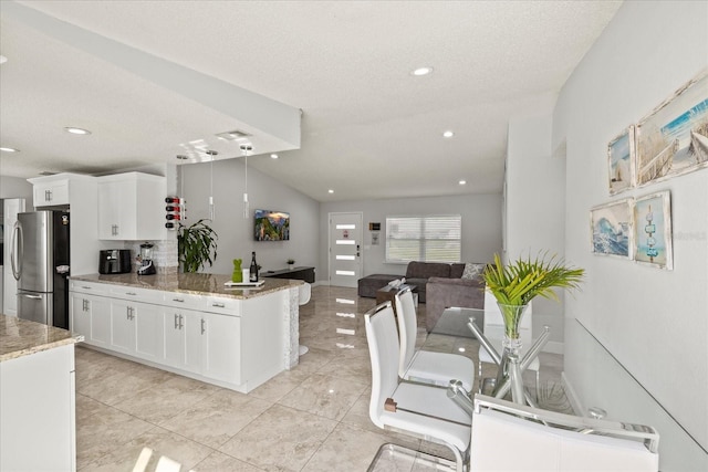 kitchen featuring freestanding refrigerator, white cabinetry, open floor plan, a peninsula, and lofted ceiling