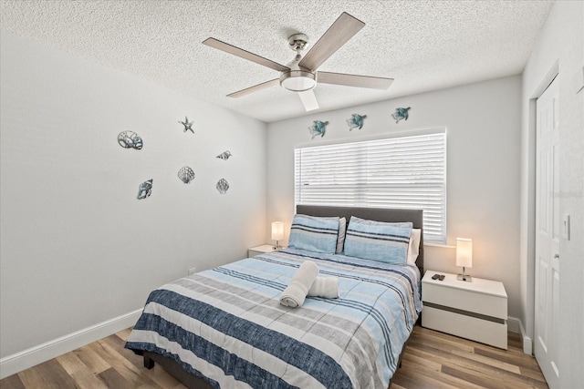 bedroom with a closet, wood finished floors, baseboards, ceiling fan, and a textured ceiling