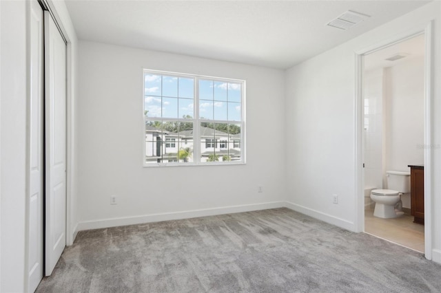 unfurnished bedroom featuring carpet floors, visible vents, a closet, baseboards, and ensuite bathroom