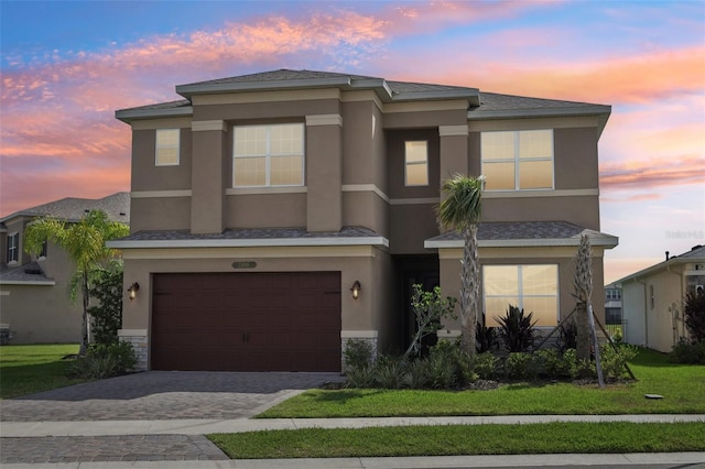 multi unit property with decorative driveway, an attached garage, a front lawn, and stucco siding