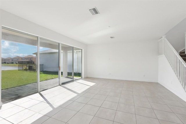 tiled spare room featuring baseboards, visible vents, and stairway