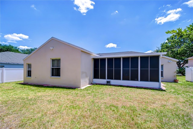 rear view of house featuring a yard, fence, a sunroom, and stucco siding