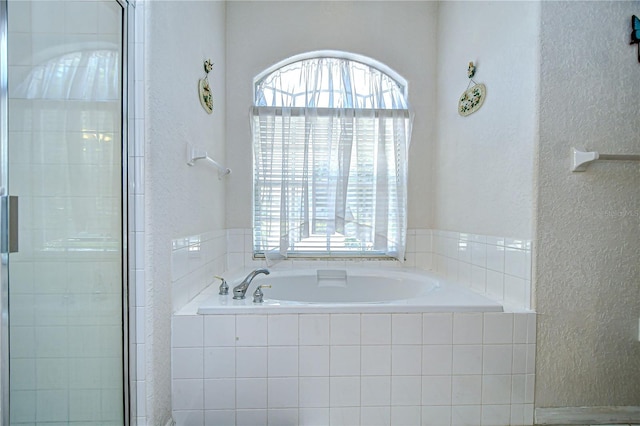full bathroom with a garden tub, a textured wall, and a shower stall