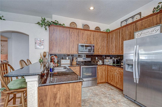 kitchen featuring a peninsula, a breakfast bar, arched walkways, a sink, and stainless steel appliances