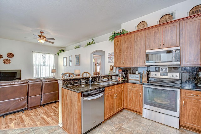 kitchen featuring appliances with stainless steel finishes, a sink, dark stone counters, a ceiling fan, and open floor plan