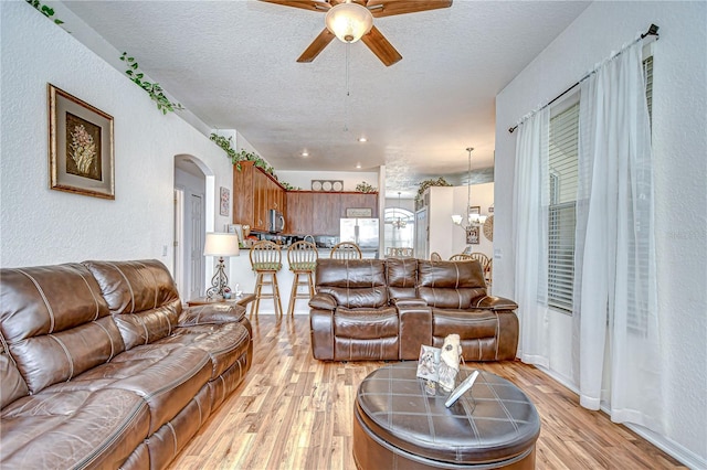 living area featuring a textured wall, light wood-style floors, a textured ceiling, arched walkways, and ceiling fan with notable chandelier