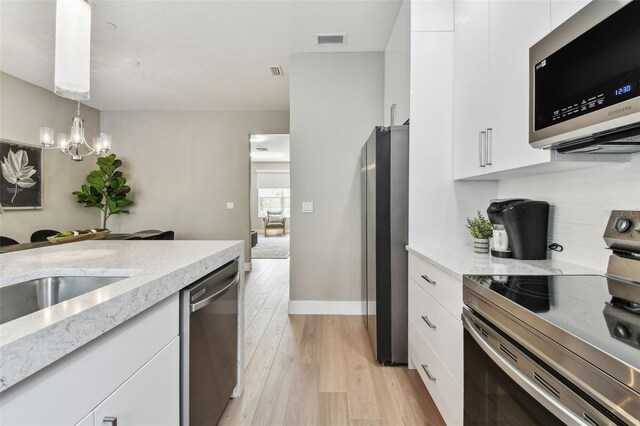 2547 Lexington Oak Dr, Brandon, FL 33511 - kitchen featuring appliances with stainless steel finishes, white cabinets, light wood-style flooring, a chandelier, and light stone counters