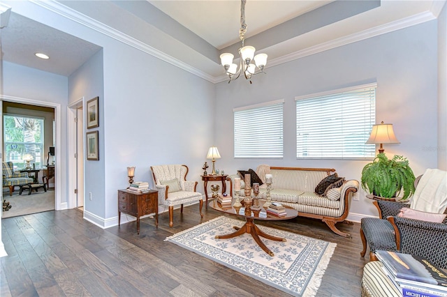 living room featuring crown molding, an inviting chandelier, baseboards, wood finished floors, and a tray ceiling