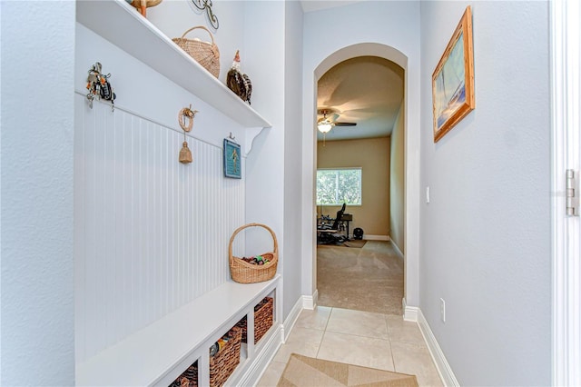 mudroom featuring a ceiling fan, arched walkways, baseboards, light carpet, and light tile patterned flooring