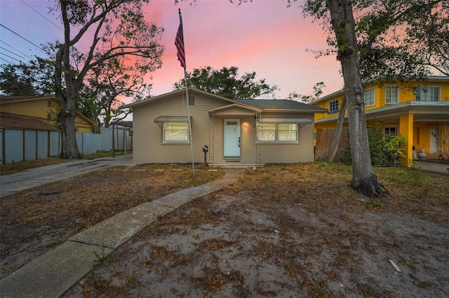 bungalow featuring concrete driveway, fence, and stucco siding