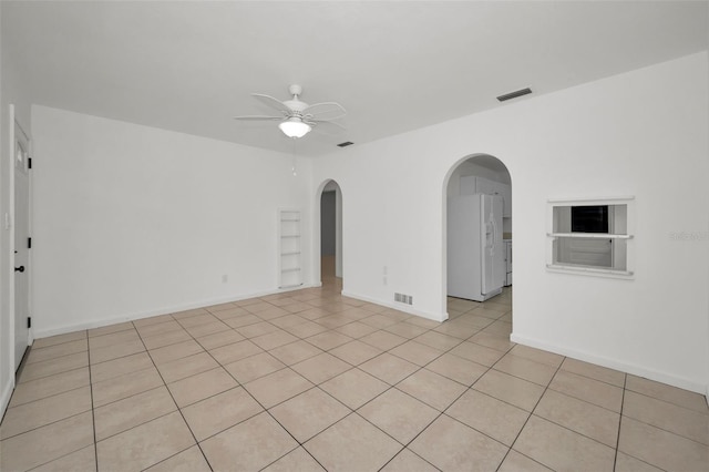 empty room featuring light tile patterned floors, baseboards, a ceiling fan, and visible vents