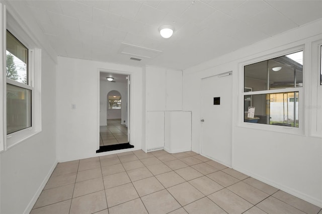 empty room featuring light tile patterned floors, arched walkways, baseboards, and visible vents