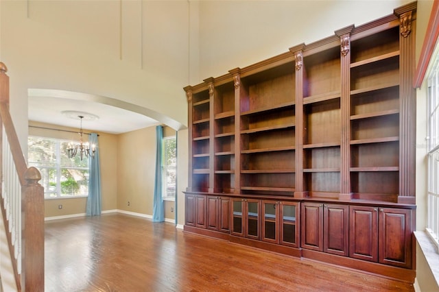 unfurnished living room featuring arched walkways, baseboards, a notable chandelier, and wood finished floors