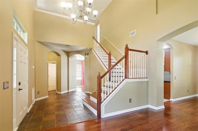 foyer featuring arched walkways, baseboards, visible vents, and a towering ceiling