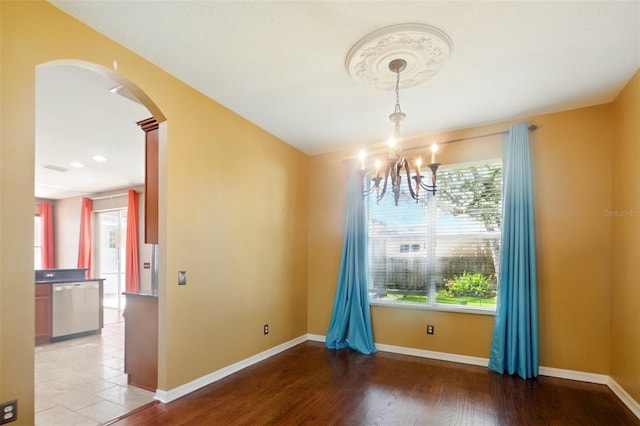 unfurnished dining area featuring arched walkways, baseboards, an inviting chandelier, and a wealth of natural light