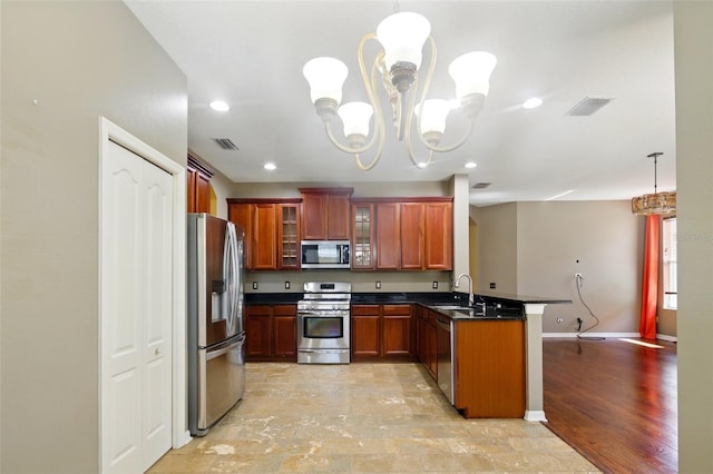 kitchen featuring visible vents, a peninsula, dark countertops, a sink, and stainless steel appliances