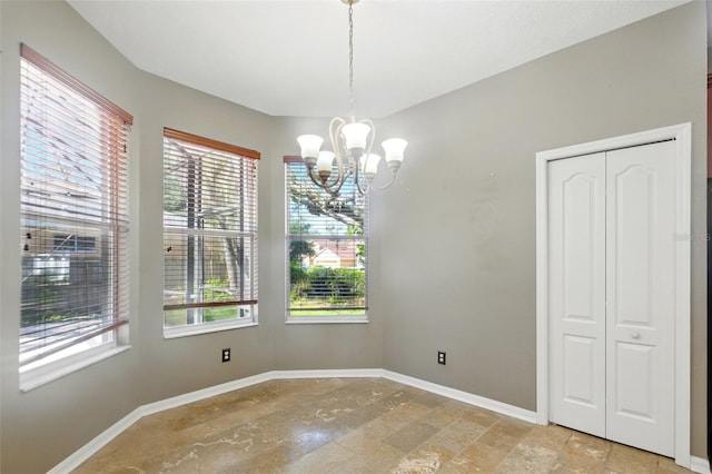 unfurnished dining area featuring baseboards, a notable chandelier, a wealth of natural light, and stone finish floor