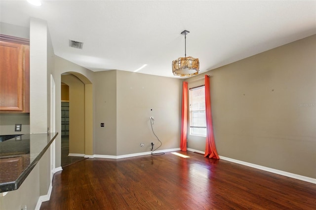 unfurnished dining area featuring visible vents, arched walkways, baseboards, dark wood-style floors, and a notable chandelier