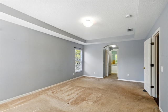 unfurnished bedroom featuring light colored carpet, arched walkways, a textured ceiling, a tray ceiling, and visible vents