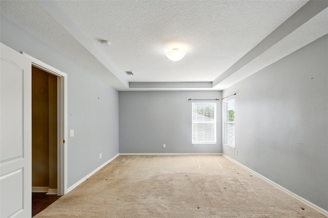 unfurnished room with visible vents, baseboards, a textured ceiling, a raised ceiling, and carpet