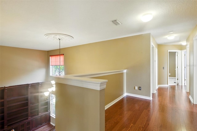 hallway with visible vents, baseboards, wood finished floors, and an upstairs landing