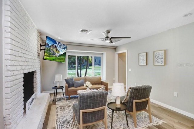 living room featuring ceiling fan, visible vents, a fireplace, wood finished floors, and baseboards