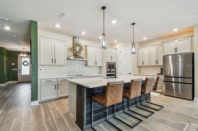kitchen with wall chimney range hood, visible vents, appliances with stainless steel finishes, light countertops, and light wood finished floors