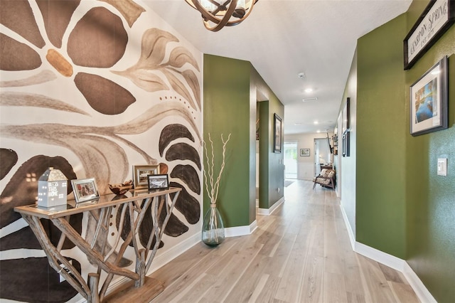 hall featuring baseboards, an inviting chandelier, and wood finished floors