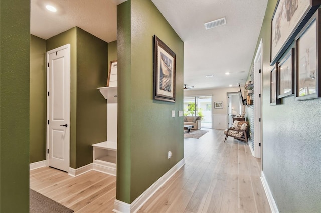 hall featuring visible vents, a textured wall, baseboards, recessed lighting, and light wood-style flooring