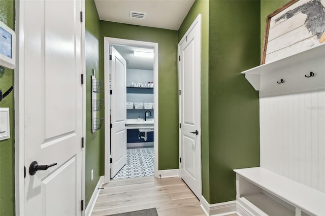mudroom featuring light wood-type flooring, a sink, baseboards, and visible vents