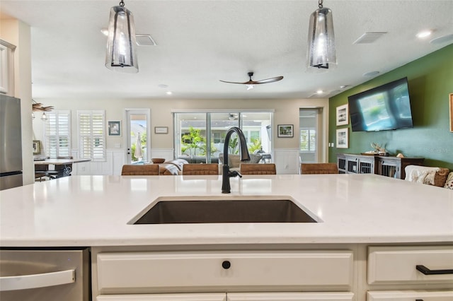 kitchen featuring ceiling fan, hanging light fixtures, a sink, light countertops, and open floor plan