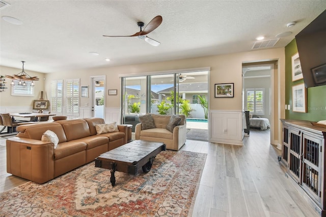 living room featuring visible vents, a decorative wall, a textured ceiling, a wainscoted wall, and a ceiling fan