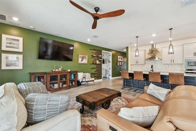 living room featuring baseboards, a ceiling fan, light wood finished floors, and visible vents