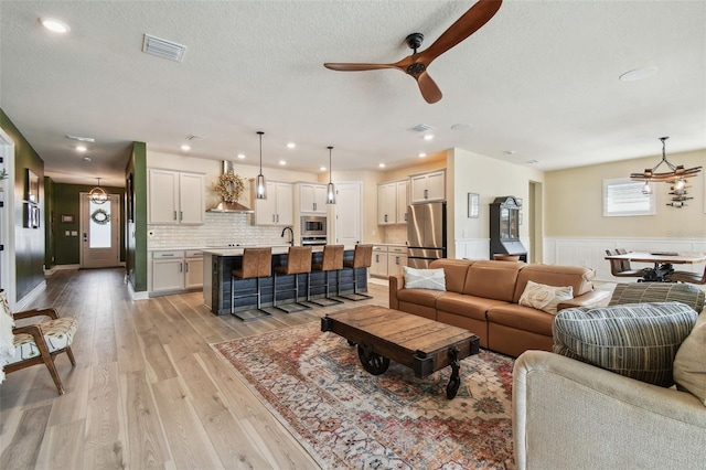 living area with ceiling fan with notable chandelier, recessed lighting, light wood-style flooring, and visible vents