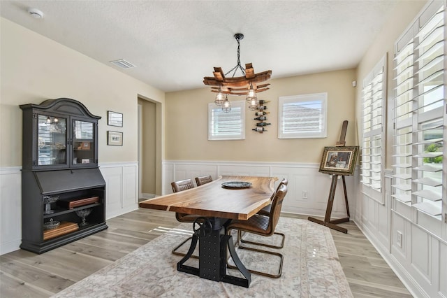 dining space featuring a wainscoted wall, light wood finished floors, a textured ceiling, and visible vents