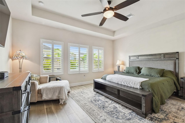 bedroom with visible vents, wood finished floors, baseboards, ceiling fan, and a tray ceiling