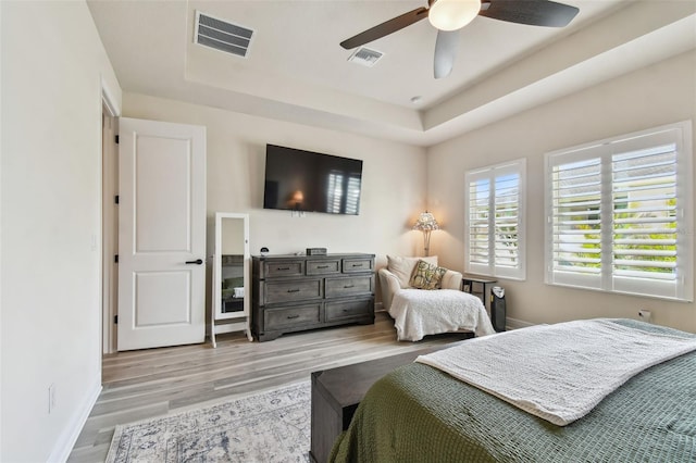 bedroom featuring a raised ceiling, baseboards, light wood-type flooring, and visible vents