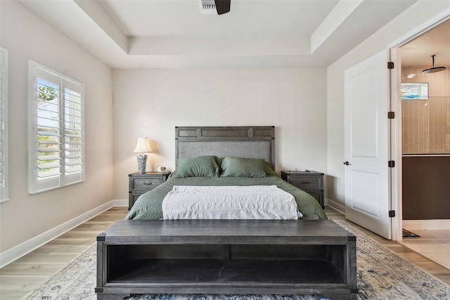 bedroom with baseboards, visible vents, a tray ceiling, and light wood-type flooring