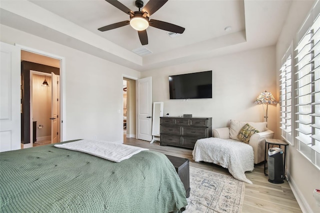 bedroom featuring baseboards, a raised ceiling, light wood finished floors, and ceiling fan