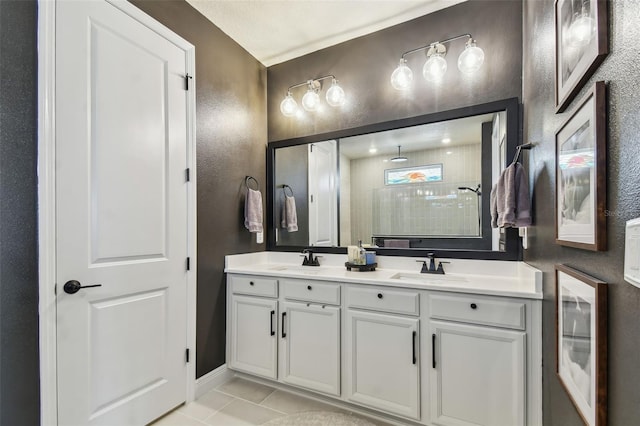 full bathroom featuring double vanity, a sink, a textured wall, and tiled shower