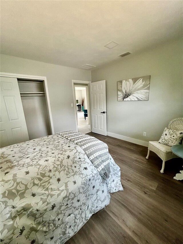 bedroom with visible vents, a closet, wood finished floors, baseboards, and attic access